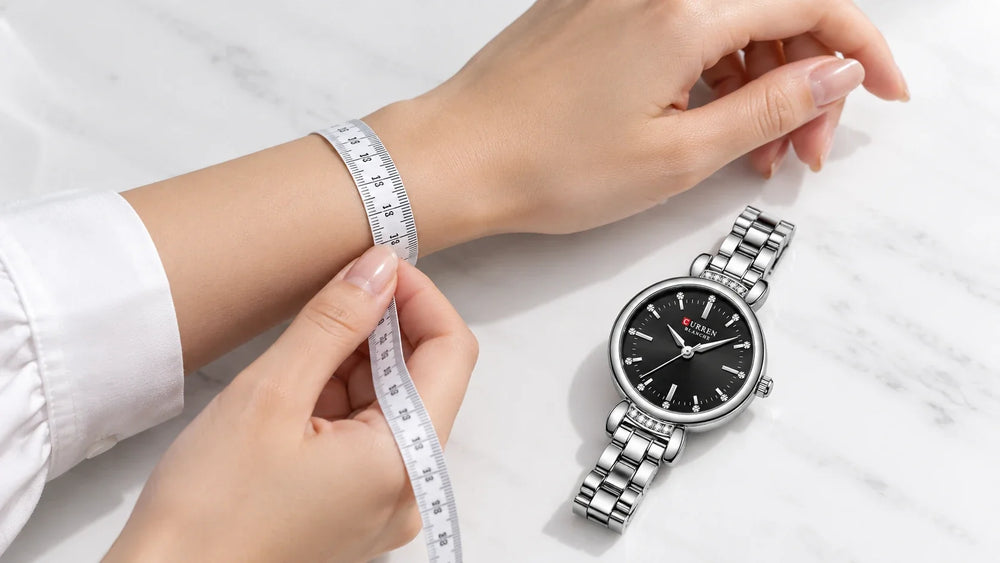 Mesure d’un poignet féminin avec un mètre souple, à côté d’une montre Minoran argentée à cadran noir.