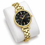 Montre Minoran 9098 dorée à cadran noir sur coussin blanc, boîtier rond et bracelet à maillons visibles