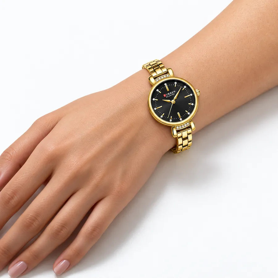 Montre Minoran 9098 dorée à cadran noir portée au poignet nu, main posée sur fond blanc