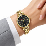 Montre Minoran 9098 dorée à cadran noir portée près d’une manche grise et d’un poignet de chemise blanc