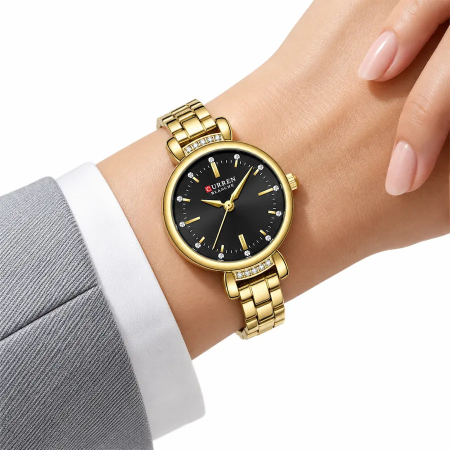 Montre Minoran 9098 dorée à cadran noir portée près d’une manche grise et d’un poignet de chemise blanc