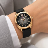Montre femme Minoran NF6111, bracelet en silicone noir et cadran noir, portée au poignet avec une veste grise